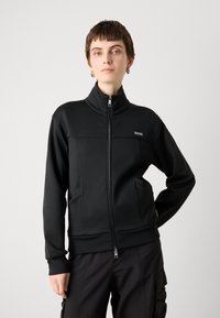 Black zip-up jacket made of smooth fabric, featuring a high collar, two side pockets, and a small "BOSS" logo on the chest.