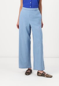 Jean large bleu clair avec une texture lisse et une taille élastique ; porté avec des ballerines léopard noires et brunes.