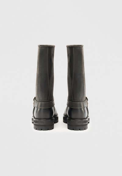 Botas de pele cinza-escuro até ao joelho, com hastes em camurça texturizada, pontas arredondadas e solas de borracha grossas; apresentam um fecho lateral e detalhes em tira.