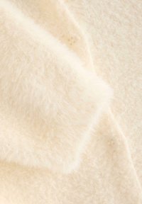 Tessuto di colore crema, morbido e peloso, con una consistenza delicata e bottoni visibili; primo piano di un cardigan che mette in mostra i suoi dettagli e il calore.