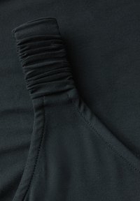 Mustan kankaan yläosa, jossa on kerätty olkainyksityiskohta ja sileä pinta. Suunnittelussa on näkyvä sauma ja tiukka siluetti.