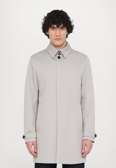 Světle šedý trench coat se strukturovanou siluetou, velkým límcem, dvěma předními kapsami a černými knoflíkovými akcenty. Hladká textura látky.