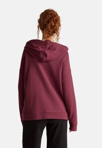 Sweatshirt à capuche bordeaux avec une coupe décontractée et des poignets côtelés, comportant une poche kangourou et un dos uni.