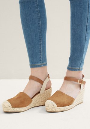 Sandales compensées en daim marron avec une semelle en jute tressé, dotées d'une sangle autour de la cheville et d'un embout arrondi. Texture lisse et couture légère.