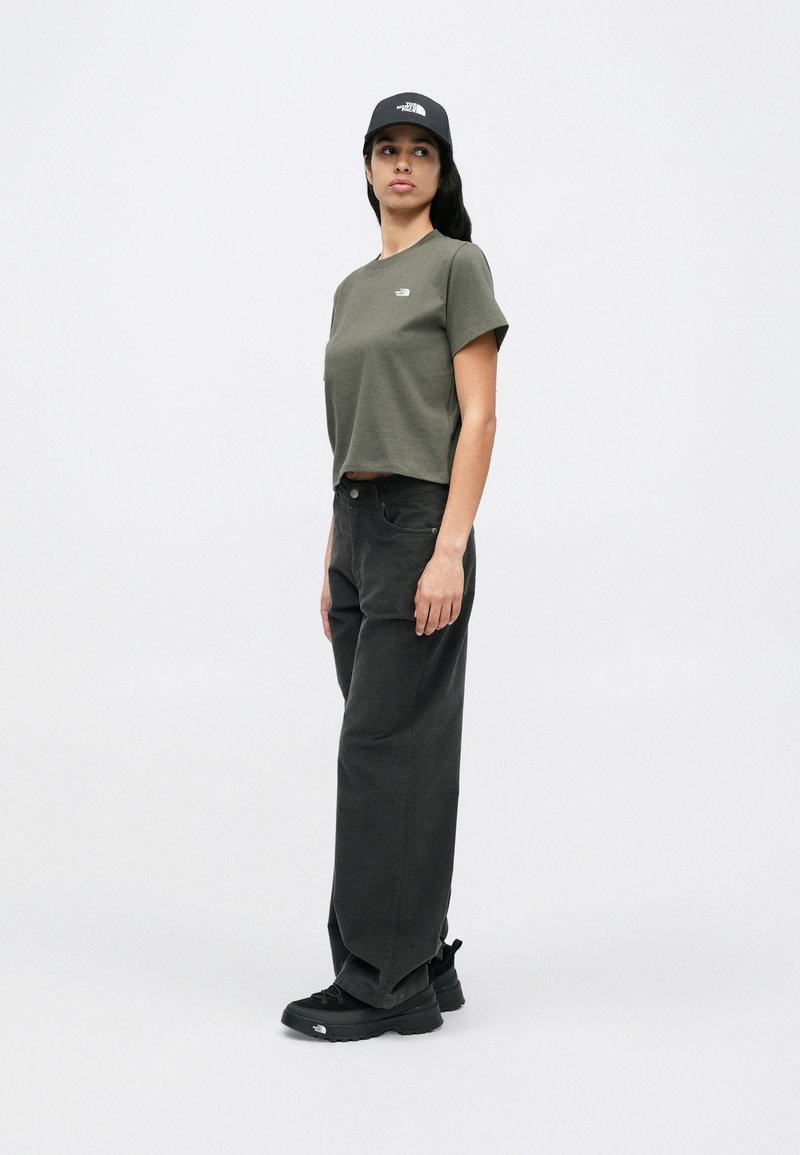 Olive green cropped t-shirt, black wide-leg pants, and black sneakers, complemented by a black cap featuring a white logo.