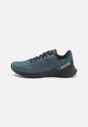 Ciemnoturkusowo-czarny outdoorowy sneaker Gore-Tex z teksturowaną podeszwą, sznurowanym przodem i wyściełanym kołnierzem, pokazany z boku na białym tle.