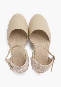 Beige kangast espadrillid ümmarguse ninaga, kootud pahkluu rihmaga ja tekstuuriga beež sisetald; lame tall mugavuse tagamiseks.