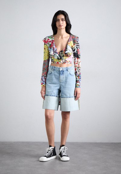 Colorful floral long-sleeve crop top with ruffled neckline, paired with light blue denim shorts featuring a raw hem and contrasting accents.