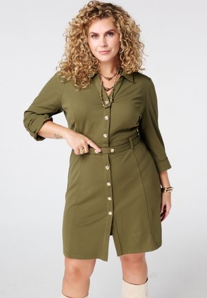 Olivengroene hemdjurk met ceintuur en kraag, voorzien van een knopen sluiting, driekwart mouwen en een lengte tot de knie. Soepele stofafwerking.