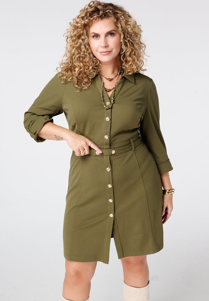 Olivengroene hemdjurk met ceintuur en kraag, voorzien van een knopen sluiting, driekwart mouwen en een lengte tot de knie. Soepele stofafwerking.