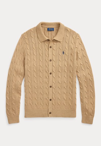 Béžový pletený sveter so vzorom vrkočov, zapínaný na gombíky, s golierom a vyšitým logom Polo Ralph Lauren v tmavomodrej farbe na ľavej strane hrude.