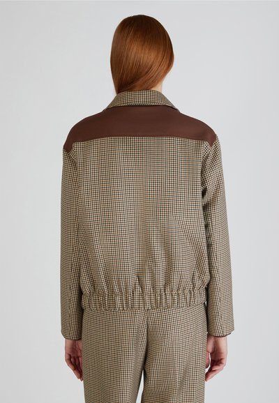 Giacca a quadri marrone e beige con una spallina in pelle marrone, vita elasticizzata e colletto, dotata di maniche lunghe.