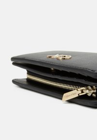 Black leather wallet with a smooth texture, gold hardware, and a zipper. Features a prominent logo detail on the front.