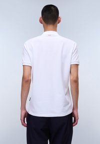 Hvid polo t-shirt med korte ærmer, en klassisk krave og tre røde accent prikker bagpå. Stoffet ser glat og blødt ud.