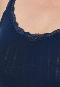 Top in navy con scollatura rifinita in pizzo, texture a coste orizzontali e un delicato fiocco al centro davanti.