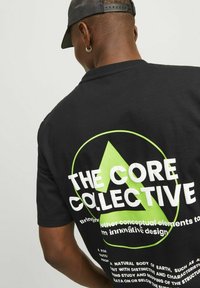 Black short-sleeve t-shirt featuring large white and neon green text on the back, with a circular design and a triangular accent.