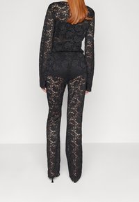 Svart spets tvådelad outfit med långa ärmar och utsvängda byxor, som visar upp intrikata blommönster och en genomskinlig textur.