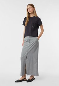Czarny t-shirt z krótkim rękawem i kieszonką, ozdobiony metalowymi oczkami, połączony z długą szaro-prążkowaną spódnicą z rozporkiem z przodu i czarnymi butami na obcasie typu slingback.