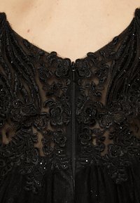 Rochie neagră cu broderie florală complicată, țesătură texturată și închidere cu fermoar ascuns la decolteu.