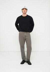 Črna majica z dolgimi rokavi, sive široke hlače, črni čevlji in bela baseball kapa s kvadratnim logotipom spredaj. Enostavna, vsakdanja obleka.