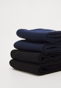 Sæt af tre rullede sokker: den øverste sok er navy, den midterste sok er mørkeblå, og den nederste sok er sort. Alle er lavet af et glat og blødt materiale.