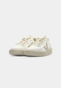 Sneakers bianchi con accenti beige, materiale superiore testurizzato, punta arrotondata, suola piatta e dettaglio del logo a contrasto sul lato.