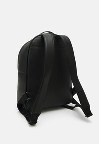 Zaino in pelle sintetica nera con una texture liscia, forma arrotondata, spallacci regolabili e maniglia superiore per il trasporto.