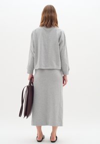 Sudadera gris y falda a juego, ambas confeccionadas con tela suave. Bolso tote marrón en la mano. Textura suave, diseño casual, silueta sencilla.