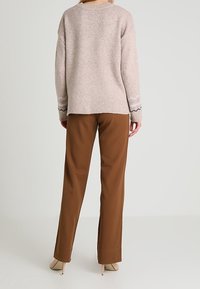 Lichtroze gebreide trui met een losse pasvorm, geribbelde halslijn en patroonmanchetten; gecombineerd met bruine op maat gemaakte broek en beige hakken.
