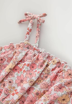 Kwiatowy top z różowymi, pomarańczowymi i żółtymi kwiatami na białym tle. Projekt wzbogacają marszczone brzegi i wiązane ramiączka.