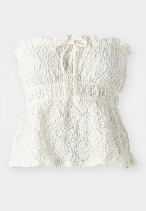 Haut blanc sans bretelles en dentelle texturée avec un corsage smocké et un ourlet froncé. Dispose d'un détail à nouer au niveau de l'encolure.