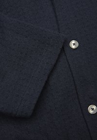 Granatowa, teksturowana koszula z widocznym zapięciem na guziki. Tkanina posiada subtelny wzór i miękką, dzianinową fakturę.