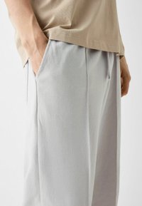 Ljusgrå sweatpants med avslappnad passform, dragsko i midjan och sidfickor. Sammanvävd med en beige t-shirt som visar en mjuk tygstruktur.