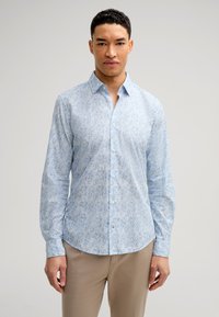 Camicia azzurra chiara con bottoni, caratterizzata da un motivo floreale in diverse tonalità di blu. Realizzata in un tessuto morbido, con maniche lunghe e colletto a punta.