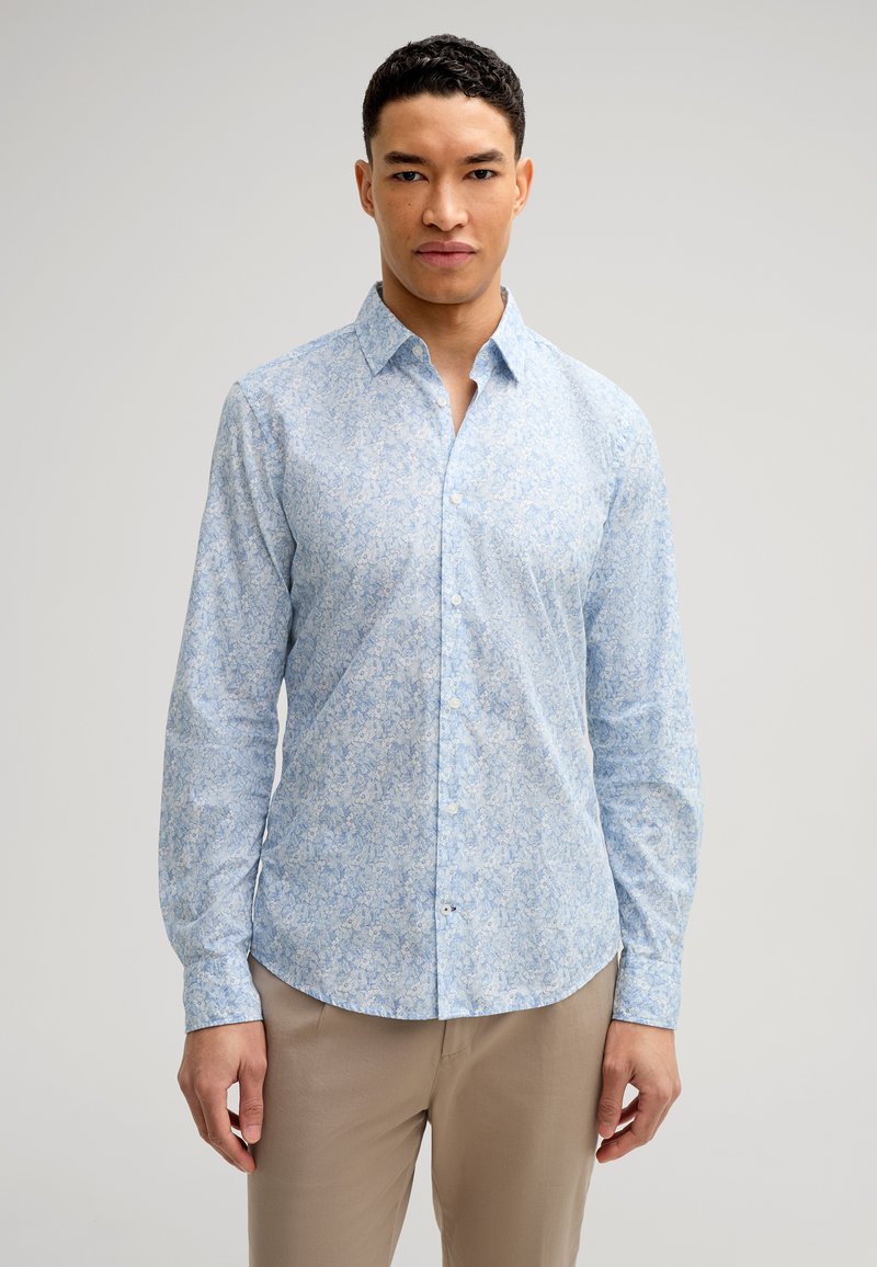 Camicia azzurra chiara con bottoni, caratterizzata da un motivo floreale in diverse tonalità di blu. Realizzata in un tessuto morbido, con maniche lunghe e colletto a punta.