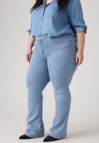 Svijetloplave traperice s visokim strukom i proširenim nogavicama, sa glatkom teksturom, prednjim džepovima i suptilnim detaljima šivanja.