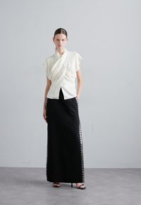 Top alb cu maneci scurte, asociat cu o fustă lungă neagră, cu embellishments argintii pe părțile laterale. Texturi netede pe întreaga suprafață.