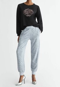 Kvinna klädd i svart sweatshirt med cirkulärt mönster och ljusgrå zebra-mönstrade joggers, i kombination med silverhöga klackar.