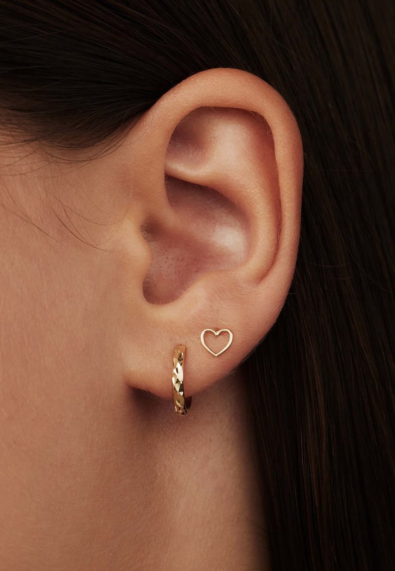 Boucle d'oreille en or avec une finition texturée et une petite boucle d'oreille en forme de cœur. Les deux boucles d'oreilles sont portées dans la même oreille.