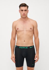 Fekete sportos boxer alsónemű zöld Nike logóval és derékpánttal. Fitted kialakítása és sima textúrája jellemzi. Állítható lábnyílásokkal rendelkezik.