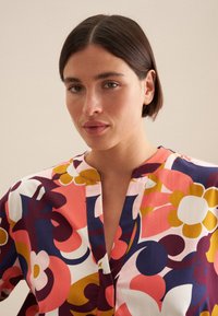 Blusa floreale colorata con una combinazione di motivi rosa, blu, giallo e bianco. Realizzata in materiale leggero con scollatura rotonda.