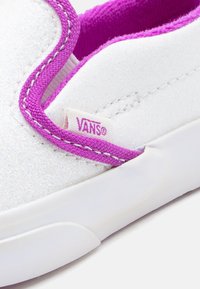 Άσπρο παπούτσι Vans με glitter λεπτομέρειες, μωβ υφασμάτινο τελείωμα και μωβ ετικέτα λογοτύπου Vans στο πλευρό κοντά στη σόλα.