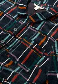 Flanelasta košulja u tamnoplavoj boji s teksturiranom površinom, s višebojnim geometrijskim uzorkom, kragnom i dugmadi sprijeda. Sadrži džep na prsima.