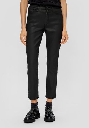 Zwarte, aansluitende jeans met een gladde textuur, middelhoge taille en ontwerp met vijf zakken. G gedragen met glanzende zwarte loafers en donkere, glinsterende sokken.