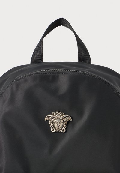Rucsac din nylon negru, cu un logo Medusa argintiu proeminent și un mâner de transport deasupra, prevăzut cu detalii texturate pe curea. Închidere cu fermoar.
