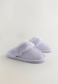 Pantofole color lavanda chiaro con un morbido risvolto in pelliccia sintetica e una texture simile alla pelle scamosciata. Presentano una suola imbottita e dettagli di cuciture bianche.