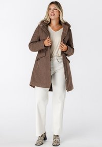 Bruine, gehoodie jas met een gestructureerde afwerking, ritszakken, gecombineerd met crèmekleurige broeken en schoenen met slangenprint. Eenvoudig, contrasterend kleurenpalet.