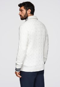 Maglione bianco a maglia con colletto alto, dotato di dettagli a righe blu e bianche ai polsini e all'orlo, tessuto strutturato.