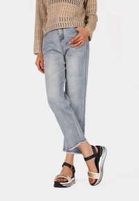 Jeans in denim blu chiaro con orlo sfilacciato; maglietta in maglia beige. Sandali platform in bianco e nero con accento in catena dorata sulla punta rotonda.