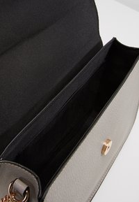 Szara torebka z syntetycznej skóry z zapięciem na zatrzask magnetyczny. Wnętrze posiada jedną przegrodę wyłożoną czarną tkaniną.